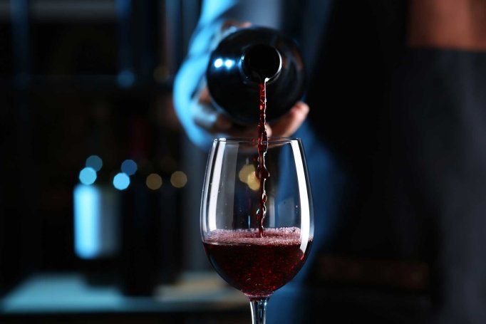 Wine is poured into a wine glass from a bottle amongst a dark backdrop.