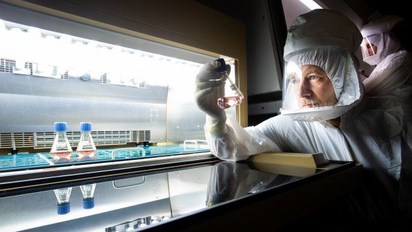 Man in full-body protective gear holding a flask in a lab