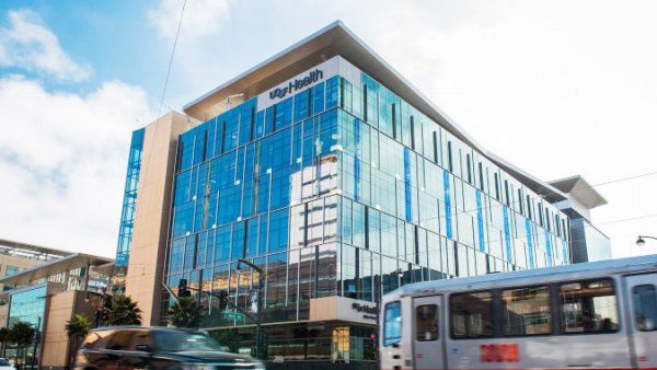 a car and a Muni train pass a UCSF building in Mission Bay