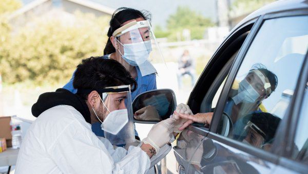 Two clinicians taking blood from a patient's hand held out of car window