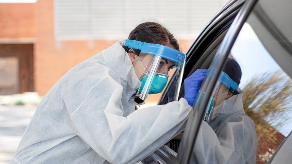 nurse wears an N95 mask and face shield while testing a person for COVID-19