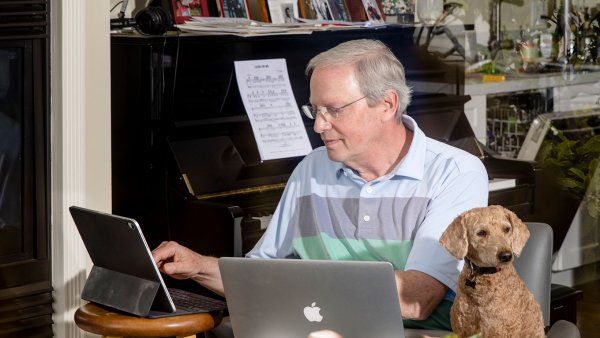 Robert Wachter, MD, sitting in his home, working on a tablet, with a computer in his lap, and his dog by his side.