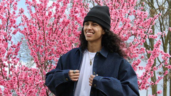 Anthony Orosco adjusts his jacket and stands in front of cherry blossom trees.