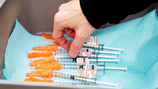 a hand reaches for a COVID-19 vaccine sitting in a tray