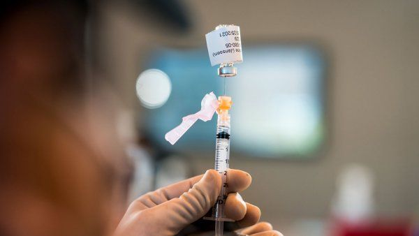 Gloved hands drawing vaccine from vial into syringe