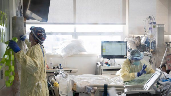 two health care workers talk with patient in a COVID-19 ICU room