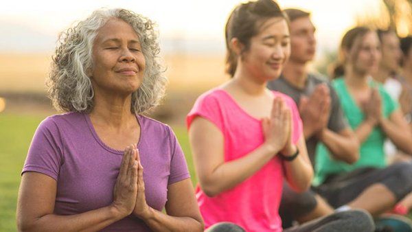 An older woman doing yoga outside with a group of people.