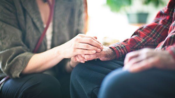 Photo of a woman holding an older man’s hand.