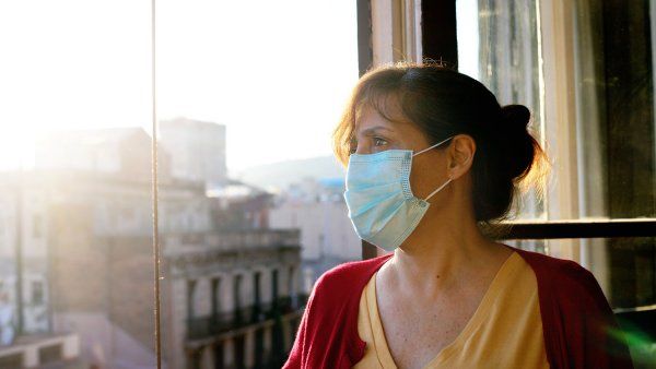 Woman wearing mask, looking out window