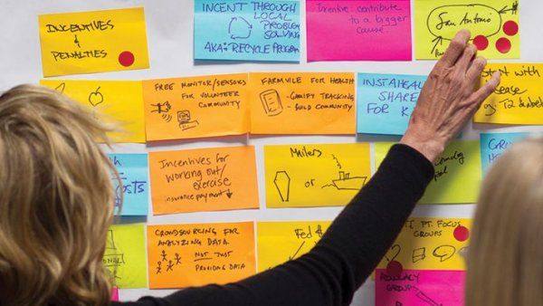 A woman points at sticky notes on a wall.