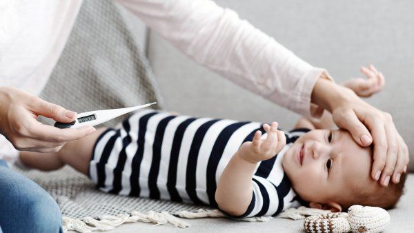 a woman holds a thermometer with one hand while holding her other hand to a newborn's forehead