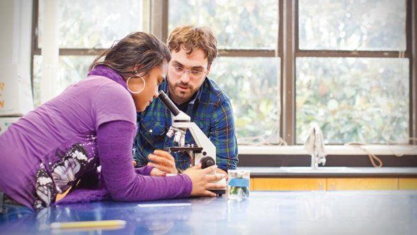 A scientist helps a high school student with a microscope.