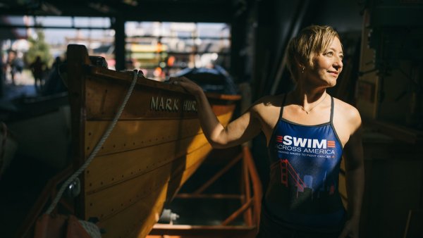 Angie Jacobson looks out of a window in a boathouse wearing a swimsuit