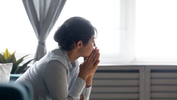 Pensive young woman sitting on couch at home looking in the distance while thinking