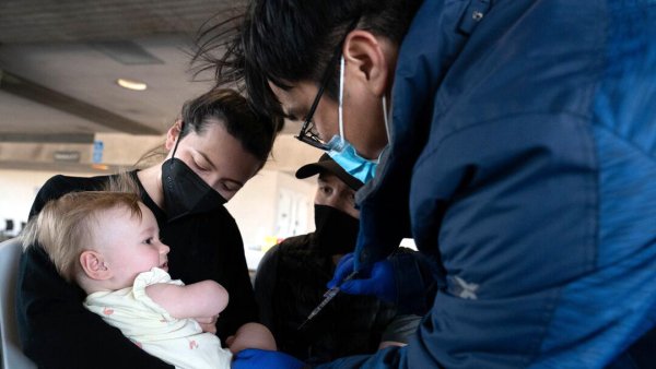 An infant receives her first COVID-19 vaccination from a UCSF nurse while being held by her parents