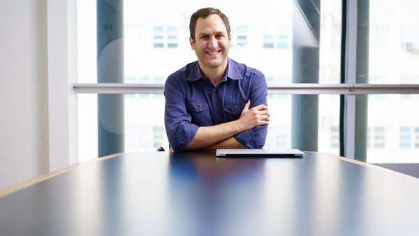 Alex Marson sitting at a table before a bank of windows