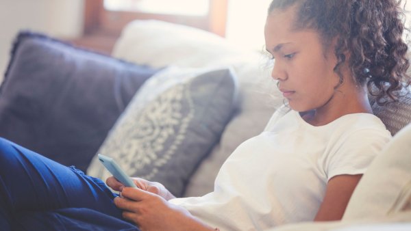 A pre-teen girl looking upset with mobile phone. She is sitting on the sofa at home.