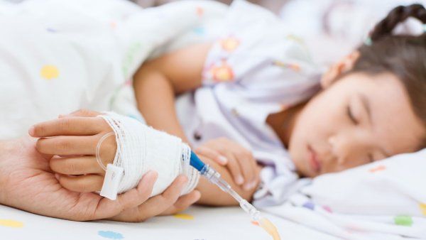 A parent holds a child's hand at a hospital