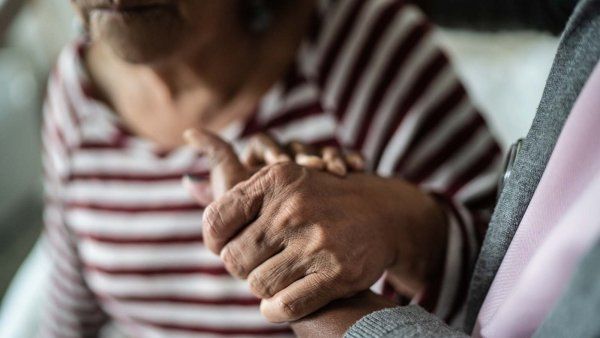 An elderly woman holds the hand of a caregiver while she gets up