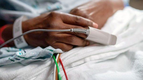 A Black hospital patient lies in bed with a pulse oximeter on their finger