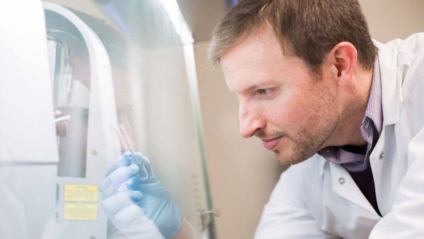 UCSF professor Kole Roybal examines a vial of liquid in his gloved hand