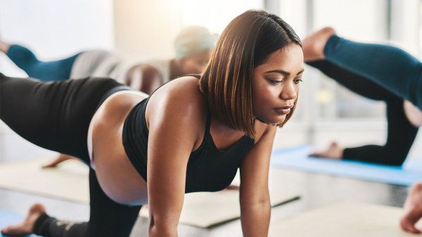 A young Black pregnant woman does exercises on a yoga mat along with other women