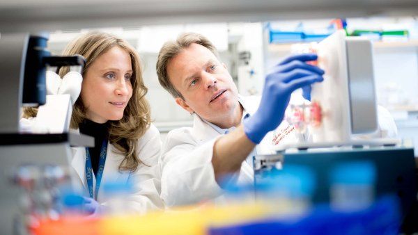 Tobias Deuse holds up an instrument in his lab while a fellow researcher looks on