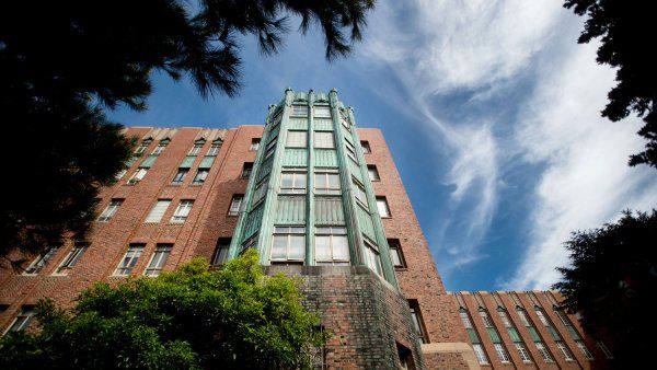 Dark trees surround an old brick building with a green facade that is home to Ward 86 at San Francisco General Hospital