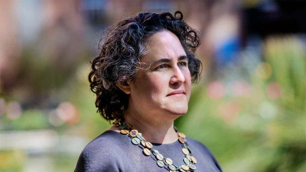 Diana Greene Foster poses for a headshot wearing a necklace. There is grass in the background