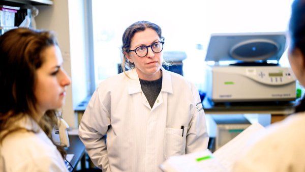 Balyn Zaro stands in her lab and speaks to two researchers. They are all wearing lab coats.