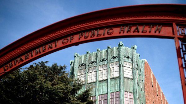 Red archway that reads Department of Health with the historic facade of a ZSFG building beyond it