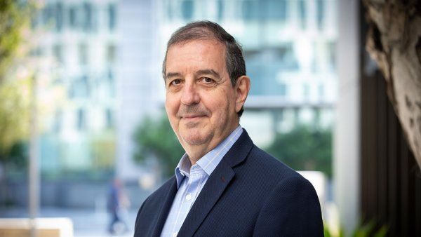 Portrait of Jaime Sepulveda wearing a dark blazer. He is standing outside, and in the background is a facade of a building and trees.