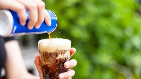 A hand pours soda from a blue can into a glass.