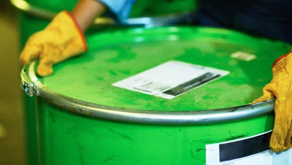 A pair of gloved hands hold a green chemical barrel.