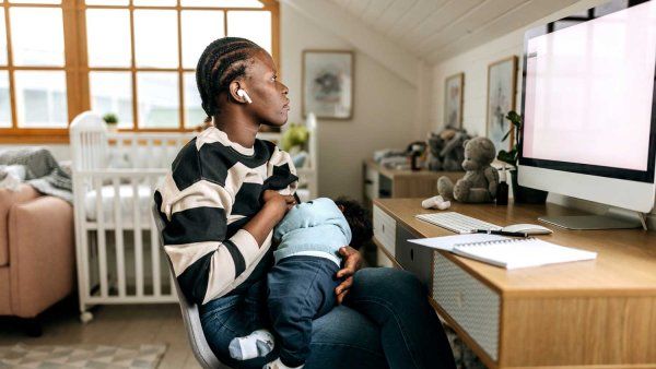 A mother working remotely breastfeeds her baby while looking at her work computer.