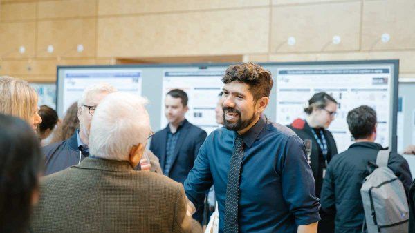 Saul Villeda speaks with attendees for the 2023 Byers Award. Behind him are scientific posters on is research.