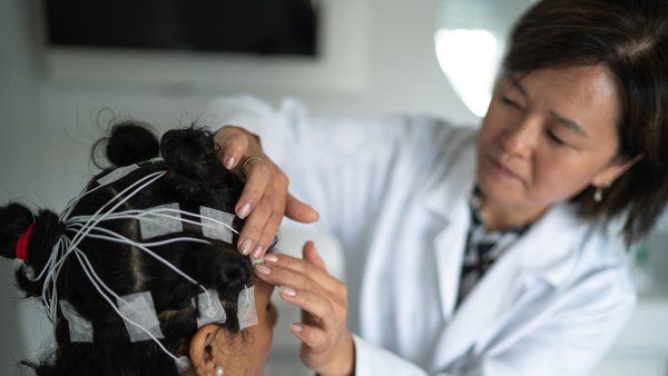 A female doctor places electrodes on a female patient's head for a sleep test polysomnography.