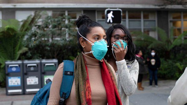 Two Black women stand outside wearing blue N95 face masks.