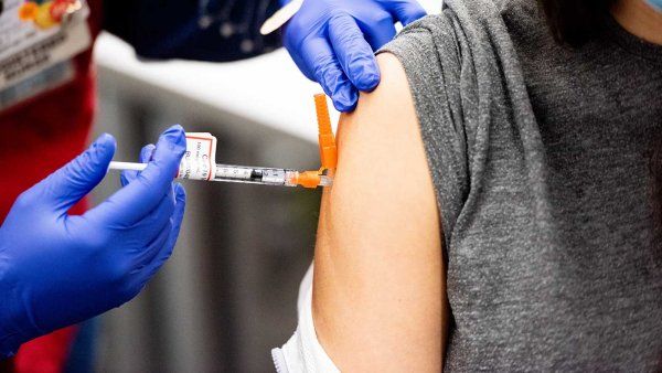 A health professional wearing a blue latex gloves delivers a COVID-19 vaccine in to a patient's shoulder.