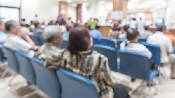 Patients sit in chairs in a crowded emergency waiting room.