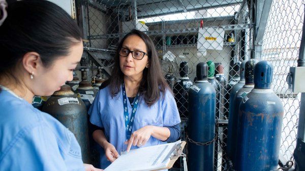 Two people talk and hold a clipboard while surrounded by nitrous oxide tanks.