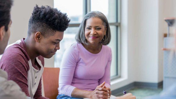 A young Black male teen smiles as he attends a group counseling session.