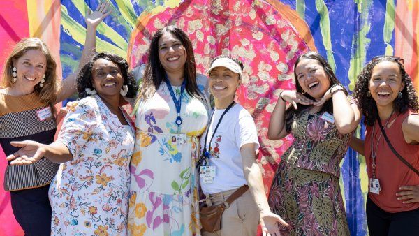 A group of women stand together and smile with their arms outstretched.