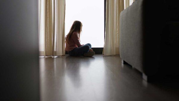 A child sits alone and stares out of a window.