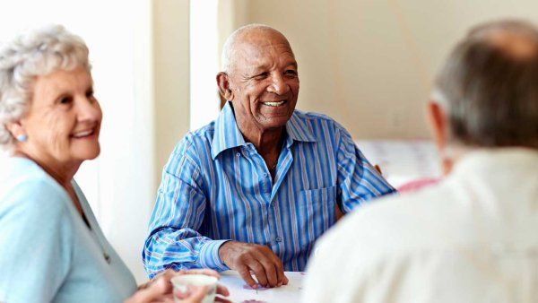 A diverse group of seniors sit together in a well-lit room at a nursing home.