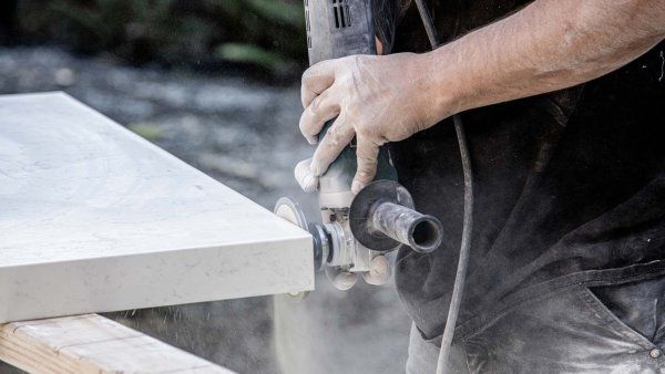 A man sands down stone for a kitchen countertop. His hands are covered in white dust from the artifiical stone.