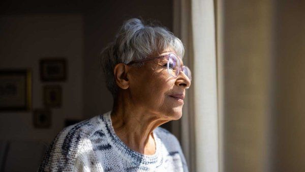 A senior woman smiles as she gazes outside a window.