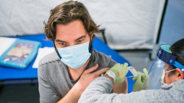 A medical professional gives a vaccine to a man wearing a surgical mask.