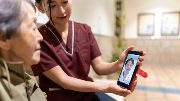 A younger woman holds out a phone so that an elderly woman can see her doctor.