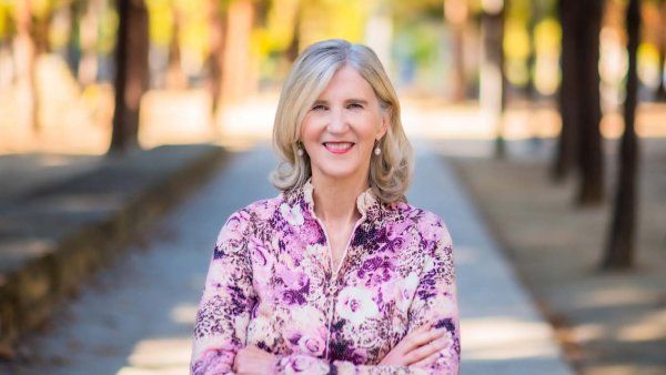 Holly Ingraham poses for a photo outdoors with trees in the background.